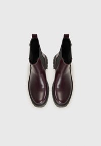 Botas de tobillo de cuero burdeos con paneles laterales elásticos, punteras redondeadas y suelas de goma negra texturizada para mayor agarre. Dos tiradores para facilitar su puesta.