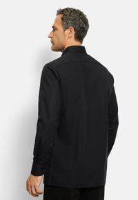 Maglietta nera a maniche lunghe con colletto classico, texture liscia, polsini con bottone e vestibilità su misura, mostrata da una vista laterale e posteriore.