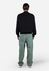 Black ribbed sweater with a high collar paired with light green baggy jeans featuring two back pockets. Simple and casual design.