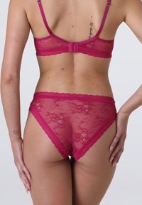 Completo di lingerie in pizzo fucsia composto da un reggiseno e una mutandina abbinata. Il tessuto è trasparente con motivi floreali e delicati bordi ondulati.