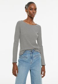 Zwart-wit gestreepte lange mouwen top met een bootnek, gecombineerd met lichtblauwe high-waisted jeans met voorzakken en een relaxte pasvorm.