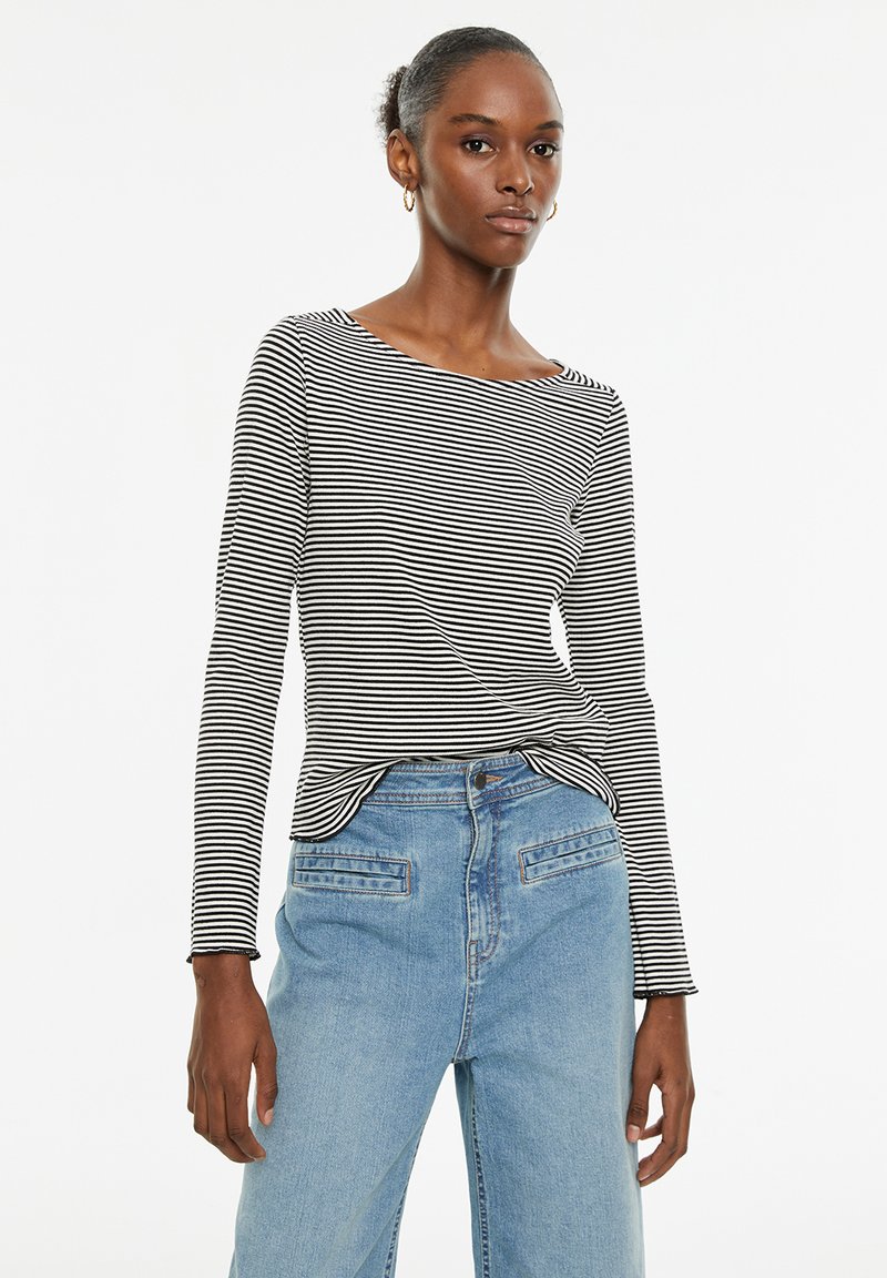 Zwart-wit gestreepte lange mouwen top met een bootnek, gecombineerd met lichtblauwe high-waisted jeans met voorzakken en een relaxte pasvorm.