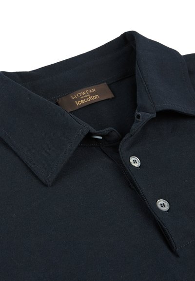 Camisa polo de algodón navy con collar clásico, tapeta de tres botones y botones plateados. La etiqueta dice "SLOWEAR icecotton". Textura suave.