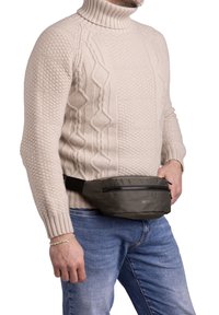 Borsetta in tessuto grigio con tasca frontale con zip, indossata sopra un maglione a trecce color crema e jeans blu. Design semplice, materiale robusto.