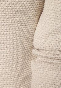 Tessuto beige chiaro con un motivo a maglia texture. Il materiale è morbido e presenta un dettaglio con orlo arrotolato su un lato.