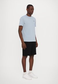 Gaiši zilas kokvilnas T-krekls ar apaļu kakla izgriezumu, saskaņots ar melniem šortiem. Baltas kedas ar diskrētām dizaina detaļām. Vienkāršs un minimālistisks stils.