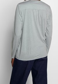 Camicia a maniche lunghe con motivo a esagoni bianco e nero, con scollo rotondo e vestibilità rilassata, abbinata a pantaloni blu scuro.