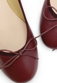 Ballerine bordeaux in pelle liscia con punta rotonda e un sottile fiocco decorativo davanti. Interno morbido color beige.