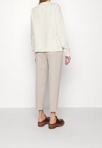 Beigový svetr s uvolněným střihem, žebrovanými manžetami a lemem. V kombinaci se světle béžovými zúženými kalhotami a hnědými botami na slip.