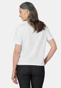 Witte katoenen T-shirt met korte mouwen en een standaard pasvorm, gezien van de achterkant, gecombineerd met donkere spijkerbroeken met decoratieve stiksels.