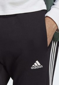 Svarta träningsbyxor med vitt Adidas-logotyp, ribbad textur och vita sidostråkar; designade för komfort och rörlighet.