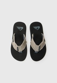 Tan fabric strap flip-flops with frayed edges, black rubber sole, and a logo on the strap. Designed for casual wear and comfort.