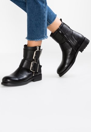 Sorte ankelstøvler i tekstureret læder med to brede spænder, båret med blå jeans med frynset kant.