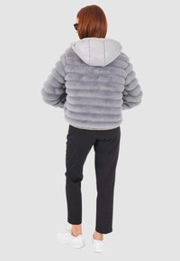 Giacca puffer grigia con texture morbida e a righe, con cappuccio lucido di un grigio chiaro. Abbinata a pantaloni a righe nere e sneakers bianche.