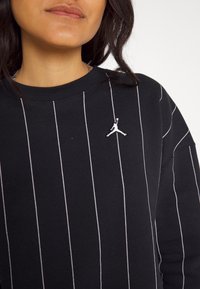 Sweatshirt noir avec rayures blanches verticales. Présente un petit logo blanc brodé sur la poitrine. Matière douce avec un col rond.