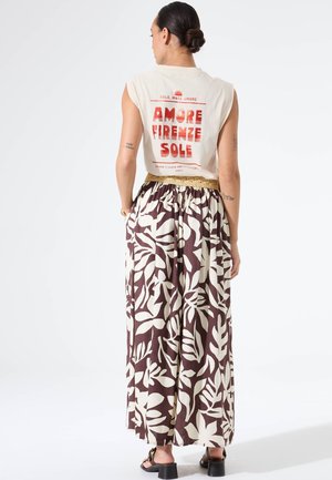 Roomwit mouwloos shirt met rode tekst, gecombineerd met een bruine rok met witte bladpatronen en een gestructureerde tailleband. Zwarte sandalen.