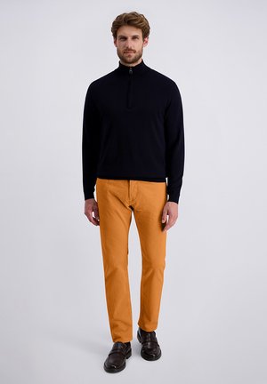 Marineblauer Zip-Neck-Pullover, orange strukturierte Hose, braune Slipper. Minimalistisches Design mit glatten und gerippten Texturen. Neutraler Hintergrund.