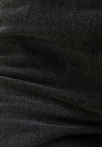 Černá denimová tkanina s texturovaným povrchem a vzorem rybí kosti. Materiál vypadá mírně opotřebovaně a má měkké záhyby.