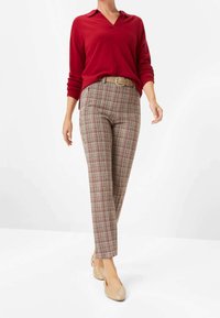 Rode trui met lange mouwen en een kraag, gecombineerd met geruite broek in beige, bruin en rood. Beige ballerina's maken de outfit compleet.