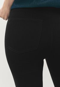 Melni denim džinsi ar pieguļošu formu. Iespējas: aizmugurējā kabata ar šuvju detaļām, gluda tekstūra un minimālisma dizains.