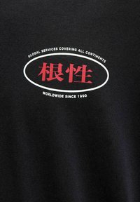 Zwarte katoenen t-shirt met witte en rode grafische tekst met een ovale omlijning. De tekst bevat details over wereldwijde diensten en het oprichtingsjaar.