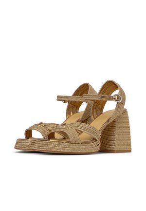 Coppia di sandali beige intrecciati con tacco a blocco, cinturini alla caviglia e fibbie argentate su sfondo bianco.