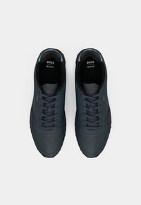 Mørkeblå sneakers med en glatt, teksturert overdel, flate snørebånd og gummisåler. Har "BOSS"-branding på tungen og sidene.