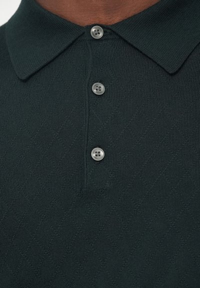 Σκούρο πράσινο πλεκτό πόλο μπλουζάκι με διαμαντένια υφή, διαθέτοντας κλασικό γιακά και τρία γκρι κουμπιά στην ταινία.