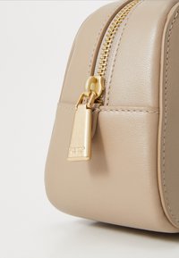 Beige leather bag with a textured finish, featuring a gold zipper and hardware. The design includes a rectangular shape and subtle stitching detail.