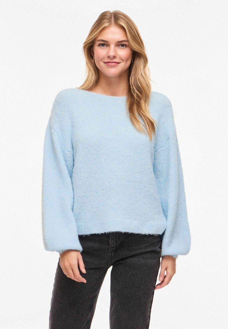 Pull oversize bleu clair avec de longues manches bouffantes et une finition texturée, associé à un jean skinny noir. Tissu doux et confortable.