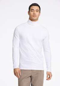 Camiseta blanca de manga larga tipo tortuga con un diseño ajustado, hecha de una tela suave. Combínala con pantalones de pana marrón. Sin patrones ni acentos visibles.