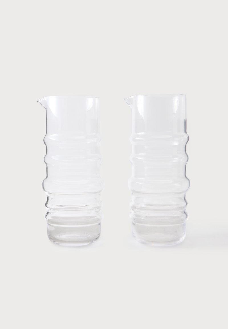 Deux pichets en verre transparent avec une texture côtelée et de petits becs verseurs, placés côte à côte sur un fond blanc.
