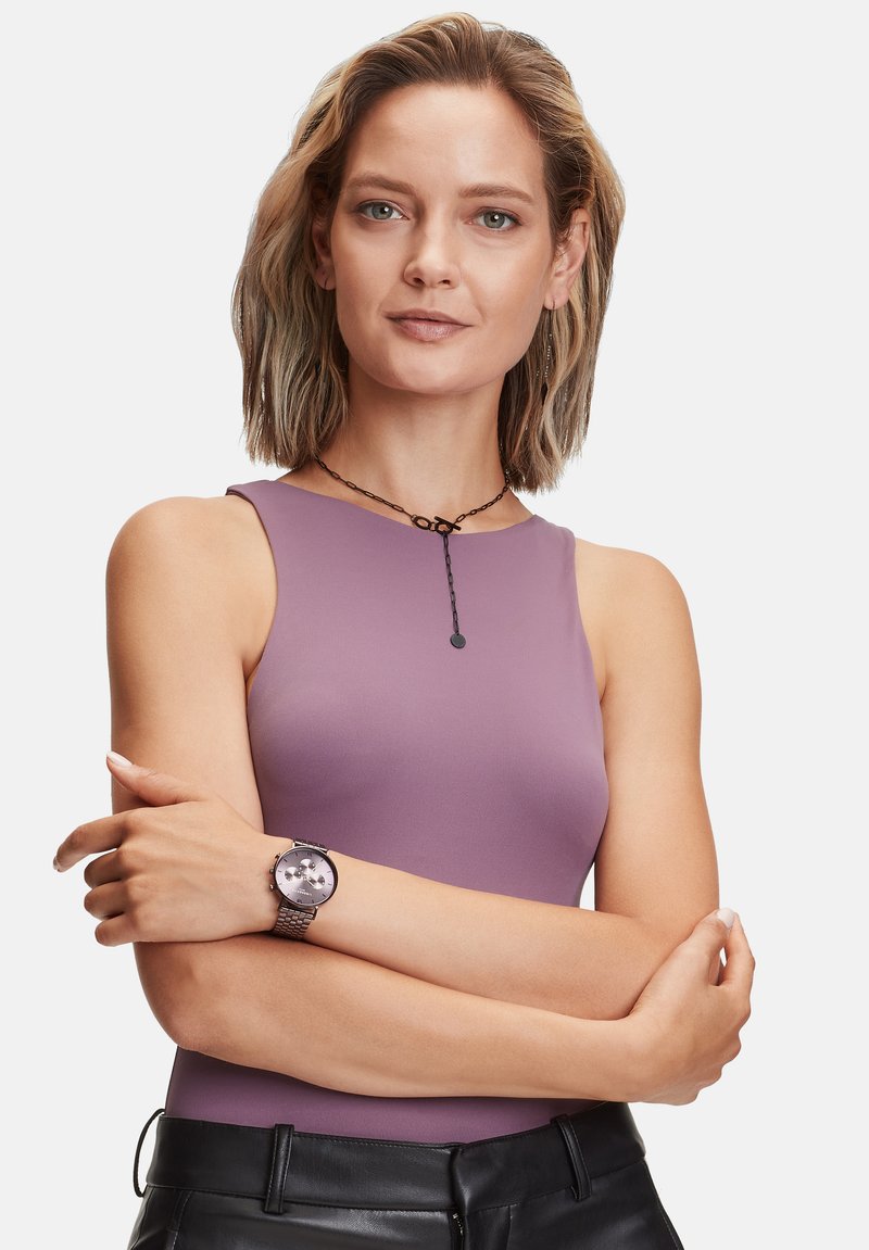 Paarse mouwloze top, gladde textuur. Zwarte horloge met een ronde wijzerplaat, zilveren accenten en een gestructureerde band, gecombineerd met zwarte aansluitende broeken.