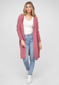 Lang rosa strikket cardigan med hette, ribbet tekstur, åpen front, kombinert med en hvit tanktop og lyseblå skinny jeans.