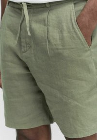 Khaki pellavashortsit rentomalla istuvuudella, joissa on kiristysnauha vyötäröllä, sivutaskut ja teksturoitu pinta.