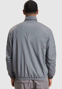 Gray lightweight jacket with a high collar, elastic cuffs, and hem, featuring a smooth texture with a relaxed fit and no visible fastenings.