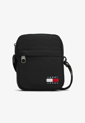 Lille sort crossbody-taske med lynlåslomme foran, justerbar rem og Tommy Jeans-logo i rød, hvid og marineblå.