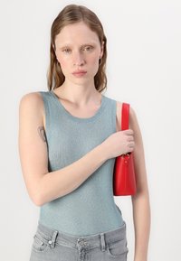 Un top in cotone leggero di colore azzurro chiaro abbinato a jeans grigi. La modella tiene una borsa in pelle rossa. Design semplice senza motivi.