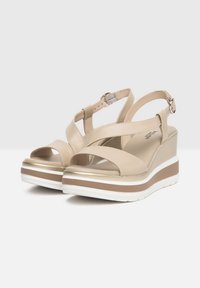 Sandales à plateforme beiges avec un design à talon compensé, dotées de lanières croisées, d'une boucle ajustable à la cheville et d'une semelle texturée blanche et marron.