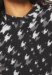 Schwarze Button-Down-Hemd mit einem Hahnentritt-Muster in Grautönen und Weiß. Verfügt über einen Kragen und ein strukturiertes Material.