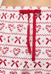 Červené a bílé pyžamové šortky s motivem cukrové třtiny a mašle, mají elastický pás a červenou šňůrku pro úpravu.
