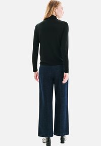 Un pull col roulé noir associé à un jean bleu foncé à jambes larges. Le jean présente une texture lisse et une coupe ajustée. Des chaussures noires complètent l'ensemble.