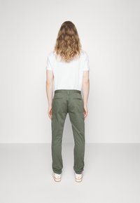 Kapsáčové kalhoty olivově zelené barvy, vyrobené z látky s hladkou texturou. Mají dvě boční kapsy a pohodlný střih. Kombinovány s bílým tričkem.