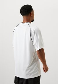 White athletic shirt with short sleeves, textured fabric, contrasting black trim along the neckline, and a relaxed fit.