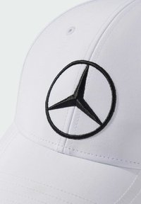 Hvid cap med et fremtrædende sort broderet Mercedes-Benz-logo i midten. Syningerne er synlige langs caps kontur.
