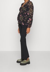 Blusa nera con fiori e maniche a sbuffo, abbinata a pantaloni neri a zampa d'elefante e mocassini chunky verdi. Fiori nei toni del rosa e del viola.