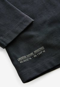 Mørkeblå riflet langærmet trøje med en sydd kant, der har hvid tekst, der står "KREATIV FREMTID INDUSTRIER" og koordinater.
