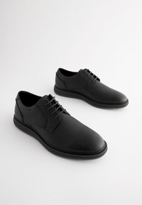 Chaussures en cuir noir à texture lisse, bout arrondi et design à lacets. Dotées d'une semelle intérieure rembourrée et d'une semelle extérieure en caoutchouc antidérapante.