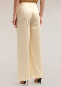 Geel wijde broek met een gladde textuur, hoge taille en twee achterzakken, gecombineerd met zwarte hoge hakken met gele accenten.