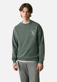 Felpa verde con collo tondo, maniche lunghe e polsini a costine. Il fronte presenta testi grafici bianchi e un design semplice. Tessuto morbido.